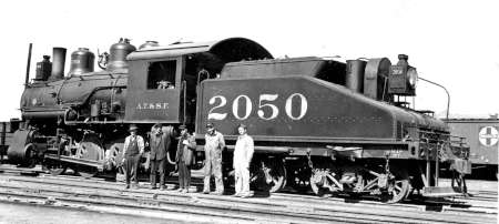 Black-and-white photo of steam locomotive number 2050 with four men standing in front and one man standing on the rear of the train.