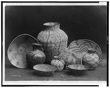 A collection of woven baskets and pots of various sizes and patterns arranged in front of a dark background.