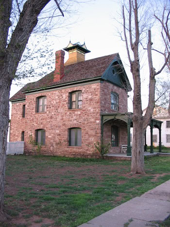 Two-story stone house with a pitched roof, brick chimney, and covered porch, surrounded by leafless trees and a patchy lawn.