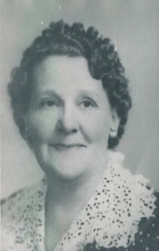 Black and white portrait of an older woman with short curly hair, wearing a blouse with a lace collar, facing the camera and smiling slightly.