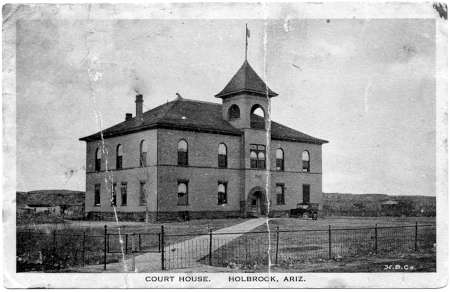 Black and white photo of a two-story courthouse with a central tower and arched entrance, surrounded by a fence. Text reads: "COURT HOUSE, HOLBROCK, ARIZ.