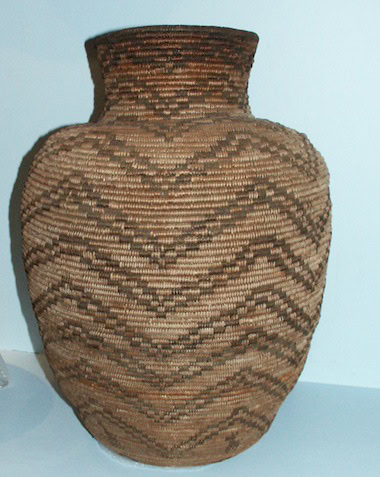 Large woven basket with a narrow neck and wide body, featuring intricate zigzag and chevron patterns in shades of brown and tan.