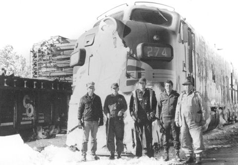 Five men stand in front of a large train engine marked 274, with snow accumulated on its front, next to a freight car labeled "S.P." on a snowy day.