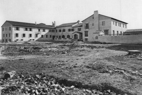 A black and white photo of a large, two-story building with a courtyard, surrounded by barren, rocky ground.