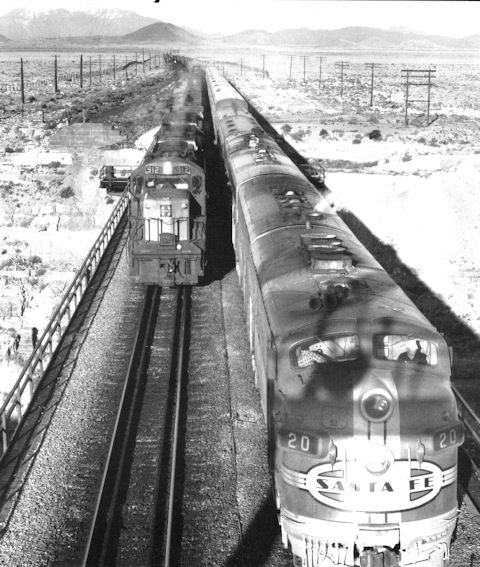 Black and white photo of two Santa Fe trains passing each other on parallel tracks in a desert landscape, viewed from above.