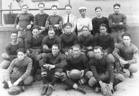 Black and white photo of a 1927 football team posing in three rows, with players in uniforms and two men in suits standing in the back. A football in front reads "1927.