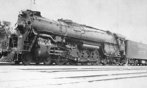 Black and white photo of a large steam locomotive and tender labeled "Santa Fe 3772" resting on railroad tracks.