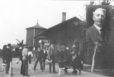 A black-and-white photo of people standing and conversing at a train station platform with a portrait of an older man in a suit inset in the top right corner.