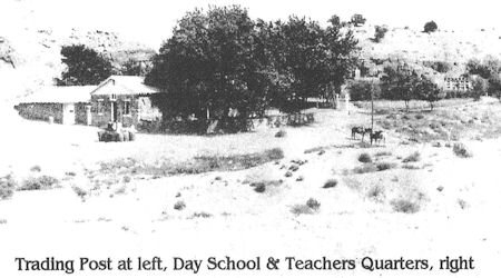 Black-and-white photo of a trading post on the left, day school and teachers’ quarters on the right, with trees and open landscape in the background.