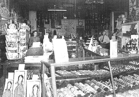 Black-and-white photo of an old-fashioned store interior with display counters, various goods, and several people behind the counter.