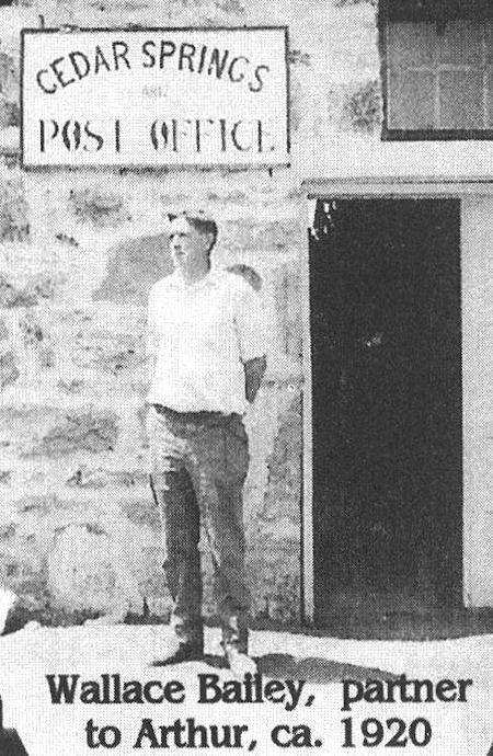 A man stands in front of the Cedar Springs Post Office. Text identifies him as Wallace Bailey, partner to Arthur, around 1920.
