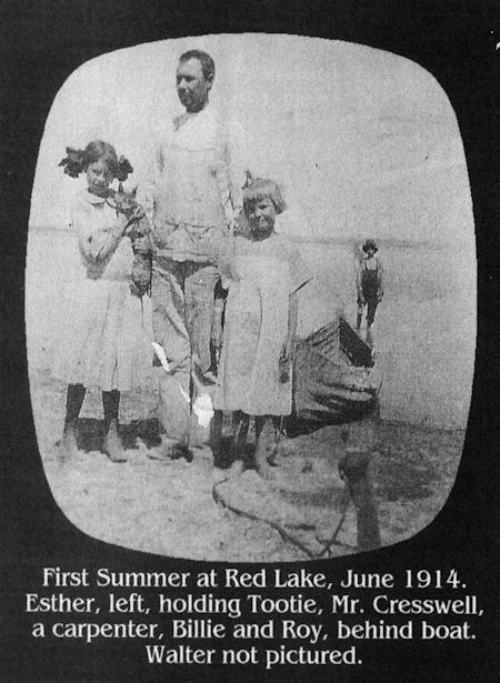 Black-and-white photo of Mr. Cresswell standing with two girls, Esther (holding a cat) and Billie, near a boat at Red Lake in June 1914.