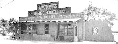 Black and white photo of the Lorenzo Hubbell Co. Trading Post, featuring a flat-roofed adobe building with signs advertising Navajo rugs and pottery.