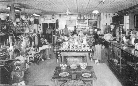 Black and white photo of a store interior with various pottery, baskets, and crafts displayed; several people stand behind the counter and among the merchandise.
