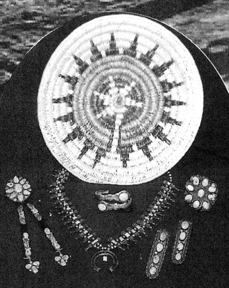 A person wearing traditional jewelry and holding a woven basket in front of their face, obscuring their identity. The jewelry includes necklaces, earrings, and a ring.