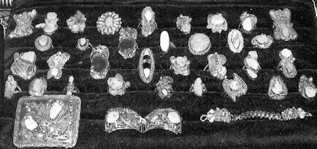 A display of assorted vintage jewelry, including rings, brooches, and bracelets, arranged in rows on a dark velvet surface.