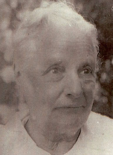 Elderly person with short, light hair and a gentle expression, wearing a light-colored top, looking slightly to the side.