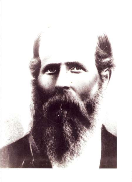 Black and white portrait of a man with a full beard, mustache, and short hair, wearing a dark jacket, facing forward with a neutral expression.