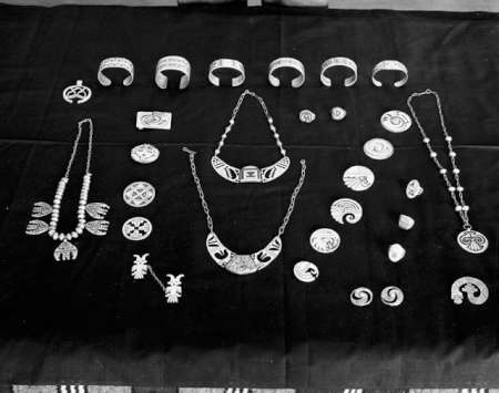 A collection of silver and beaded jewelry, including necklaces, bracelets, rings, pendants, and brooches, arranged neatly on a dark cloth.