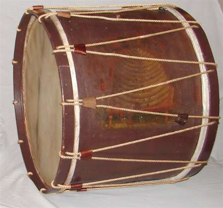 A large cylindrical drum with a wooden body, rope tensioning, and parchment drumheads on both sides, placed on a white surface.
