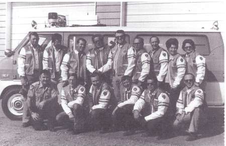 Black and white photo of a group of people in uniform jackets posing in front of a van with emergency lights on top.