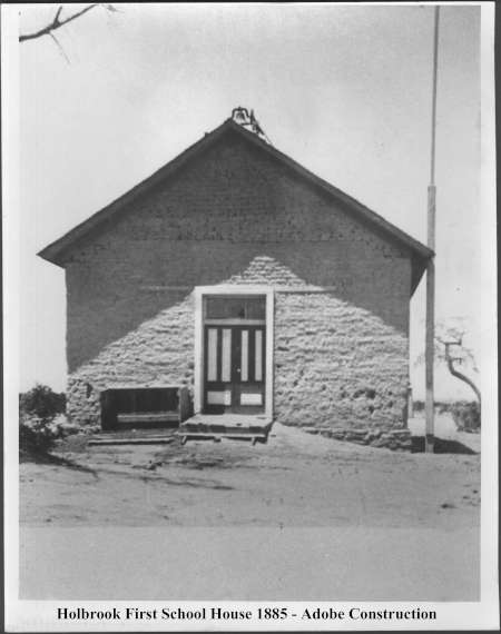 Black and white photo of a small adobe schoolhouse with a central door and two windows, labeled "Holbrook First School House 1885 - Adobe Construction.