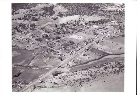 Aerial view of a small rural town with scattered houses, roads, and patches of farmland surrounded by trees and open fields.