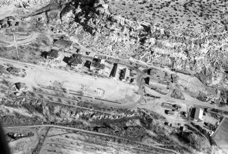 Aerial view of a small settlement with several buildings, dirt roads, and rocky terrain surrounding the area.