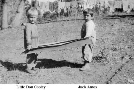 Two young children stand outdoors holding a large flat object. Laundry hangs on clotheslines in the background. The names "Little Don Cooley" and "Jack Amos" are labeled below each child.