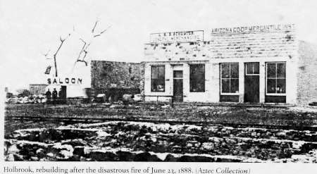 Black and white photo of Holbrook buildings after the June 22, 1888 fire, showing damaged saloon and Arizona Coop Mercantile store with debris in front.