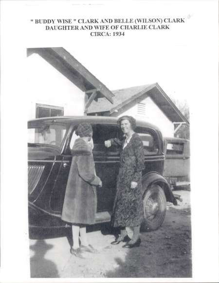 Two women stand beside a vintage car in front of a house. The image is labeled as being from 1934, showing Belle Clark and her daughter.