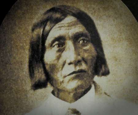Sepia-toned portrait of a Native American man with straight, chin-length hair, wearing a light-colored shirt and looking slightly to the side.