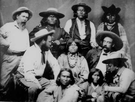Black and white historical photo of a group of men and two children, some wearing hats and traditional clothing, posing for a portrait.