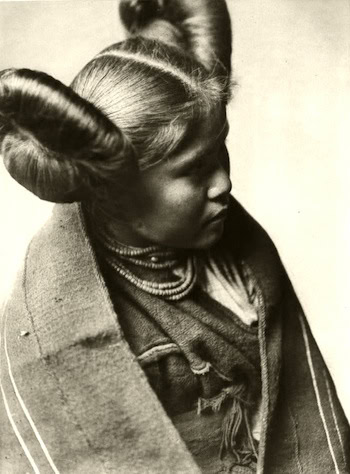 Black and white photo of a young woman in traditional clothing, with hair styled in two large coiled buns on each side of her head.