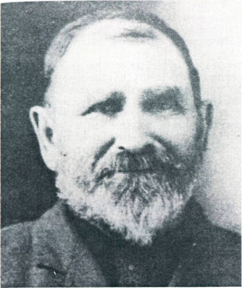 Black and white portrait of an older man with a full beard, short hair, and wearing a jacket.