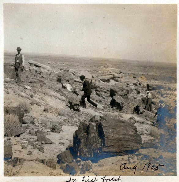Three people walk among large rocks and sparse vegetation in a barren, rocky landscape. The photo is dated August 1905 in handwritten text.