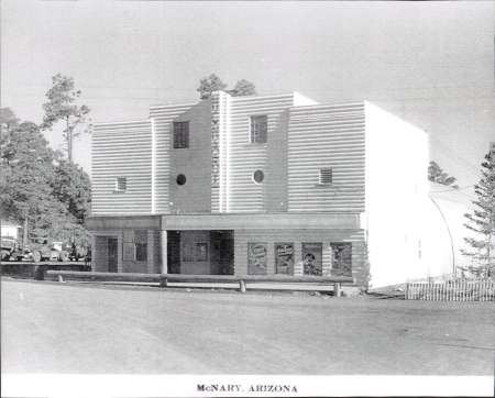 Black and white photo of a two-story building with circular windows in McNary, Arizona, surrounded by trees and a road in front.