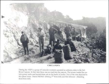 Black and white photo from the 1920s showing miners working at an asbestos mine in a rocky area, with sacks and mining equipment visible in the foreground.