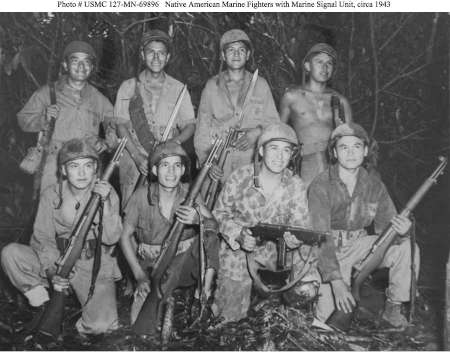 Eight Native American U.S. Marines pose with rifles and gear in a jungle setting, identified as a Marine Signal Unit, circa 1943.