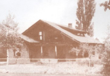 Sepia-toned photo of an old wooden house with a gabled roof, surrounded by trees and a low fence.