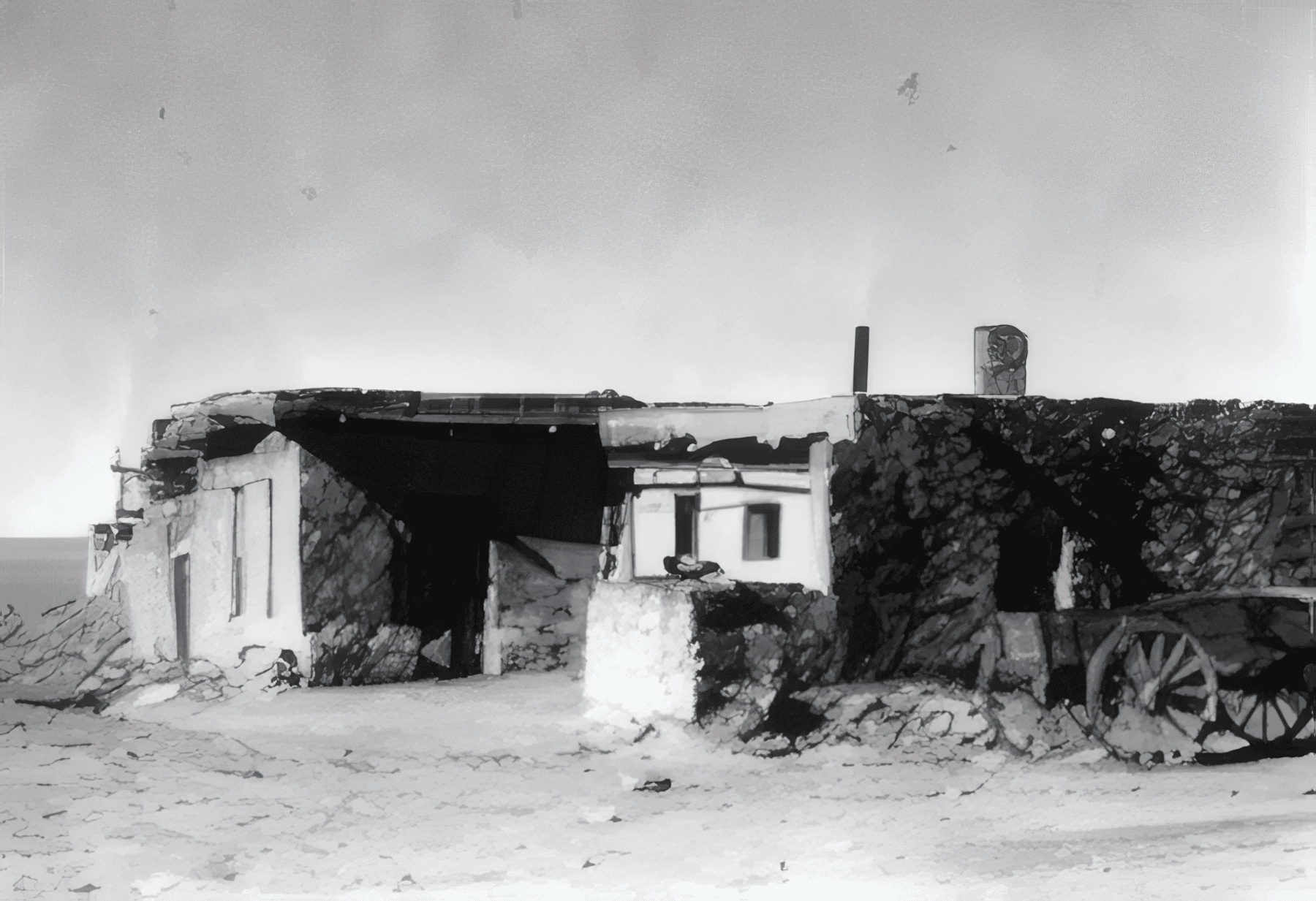 a weathered adobe building with a flat roof stands in a barren landscape, accompanied by an old wooden wagon wheel in the foreground.