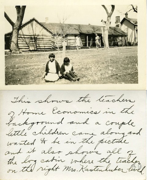 Two children sit on the grass in front of a log cabin. Handwritten text below explains the scene, mentioning teachers of Home Economics and identifying the cabin and people.