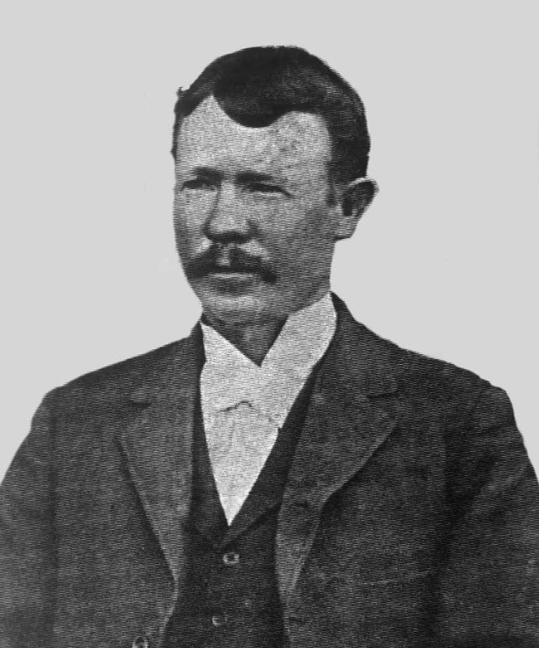Black and white portrait of a man with a mustache, wearing a suit and vest, facing forward against a plain background.