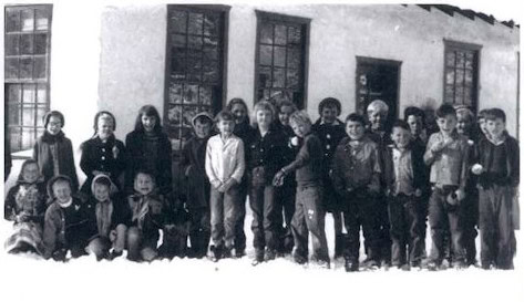 A group of children pose for a photo in front of a building with multiple windows, dressed in winter clothing.