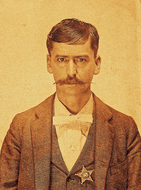 Sepia-toned portrait of a man in a suit with a bow tie and a sheriff's badge pinned to his vest, looking directly at the camera.