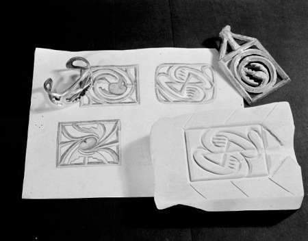 Metal stamp, ring, and clay impression are displayed on a sheet with geometric graphic designs, showing the process of creating patterns.