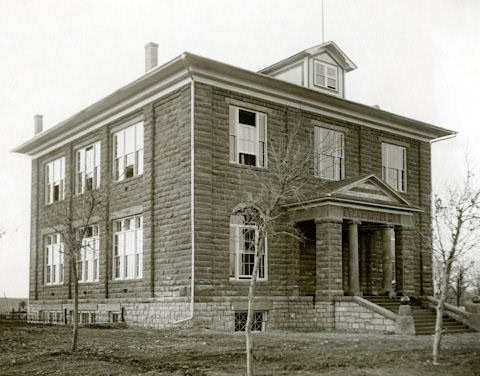 Two-story stone building with large windows, a columned entrance, and leafless trees in front; early 20th-century architectural style.
