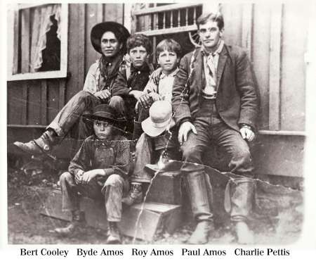 Five boys sit and kneel on the steps of a wooden building, posed for a group photograph. Names are labeled below each boy: Bert Cooley, Byde Amos, Roy Amos, Paul Amos, Charlie Pettis.