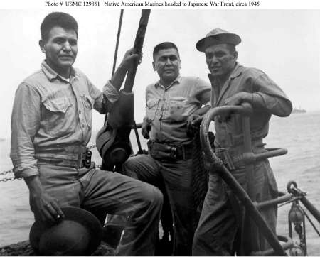 Three Native American US Marines in uniform stand on a ship’s deck, leaning on equipment, heading to the Japanese War Front, circa 1945.